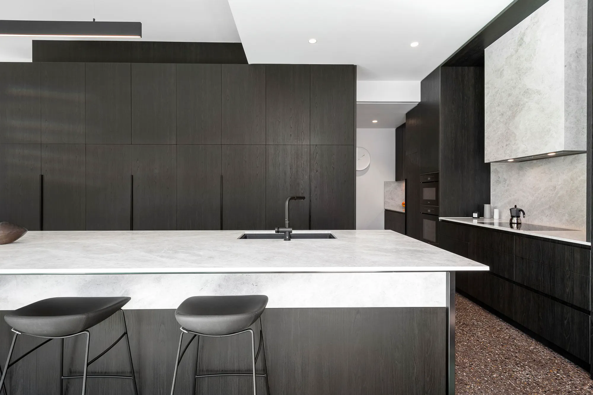 Dark timber kitchen with a waterfall stone island and black stools