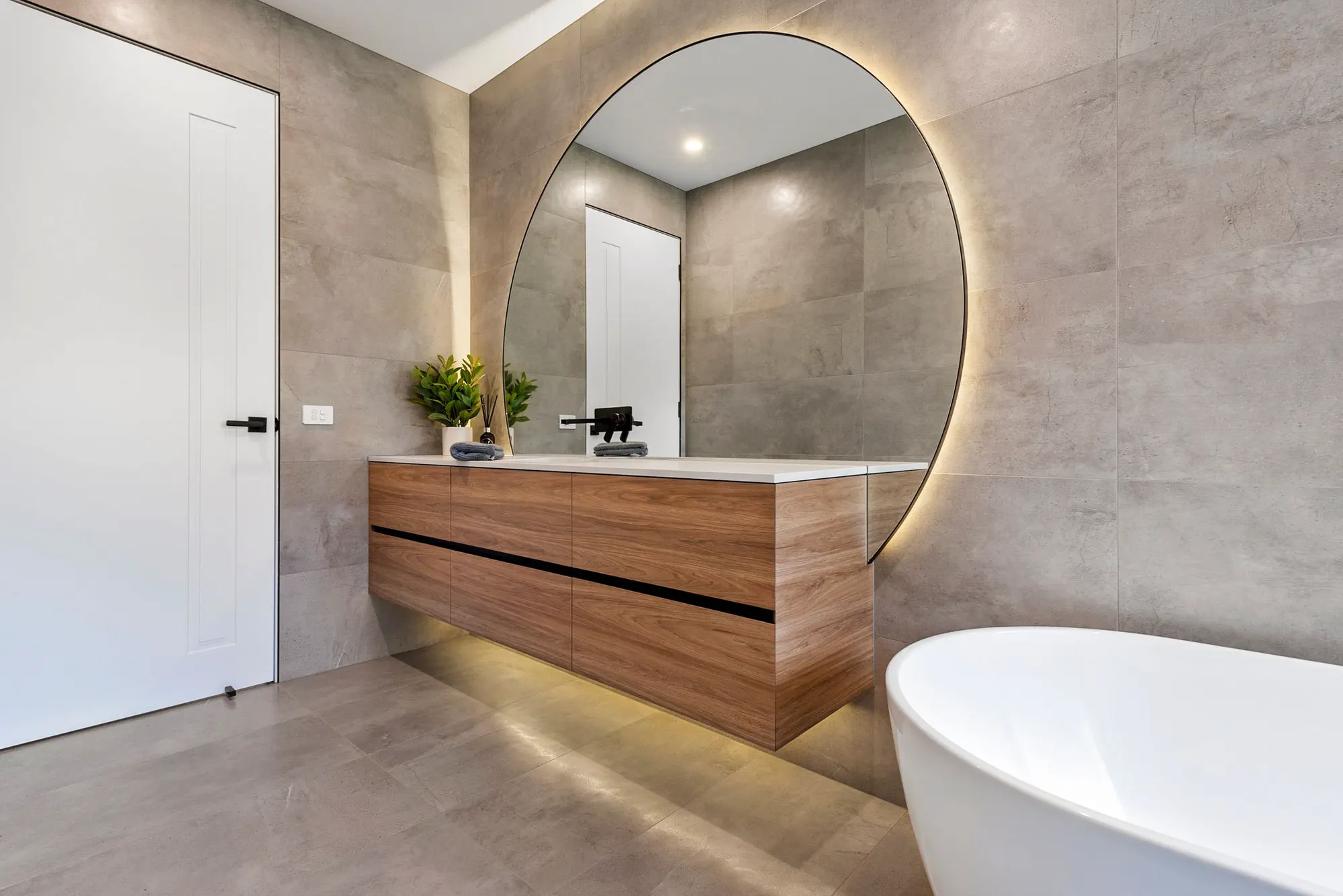 Bathroom with a timber vanity, round backlit mirror and freestanding bath