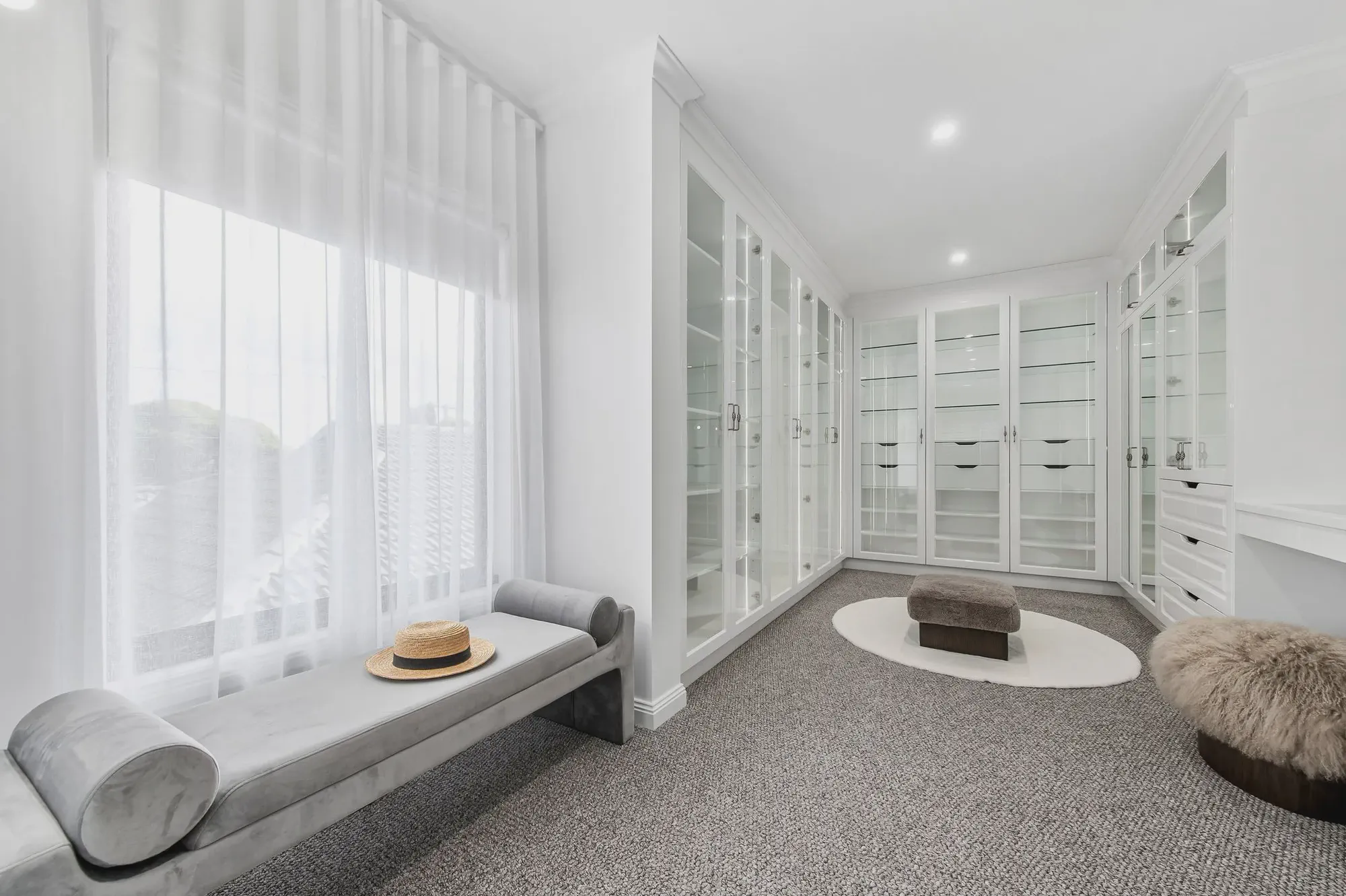 White walk-in robe with glass-fronted cabinets and a window seat