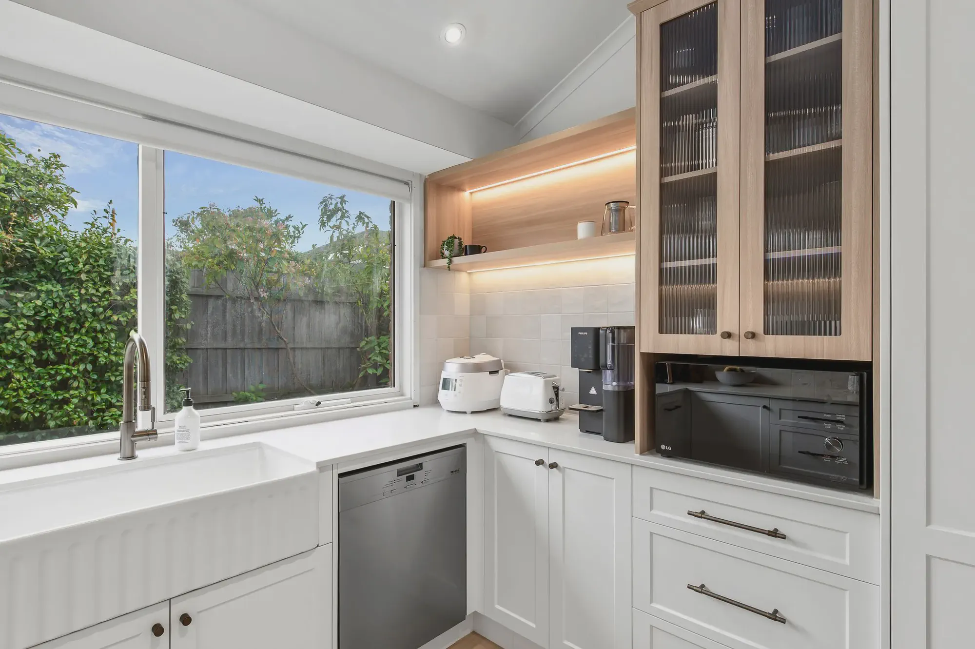 White shaker kitchen with timber floors and a garden window